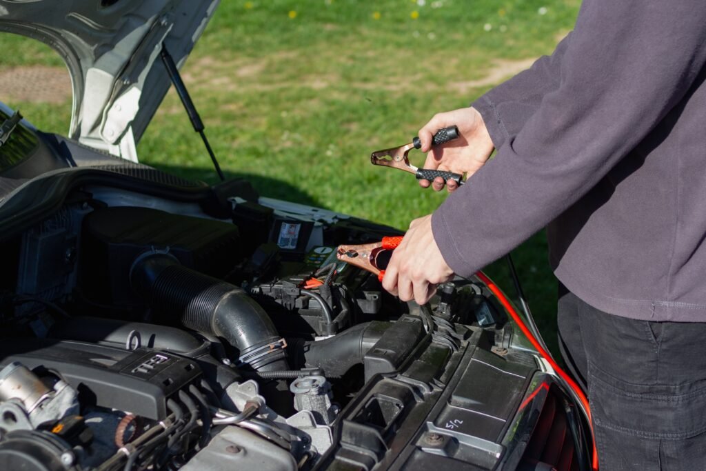 Person connecting jumper cables to a car battery under the open hood